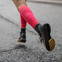 Löpare i korallfärgade Run Performance Compression Sleeves på asfalt