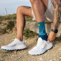 Person sitter på en sten och drar upp Sports Achilles Support över fotleden
